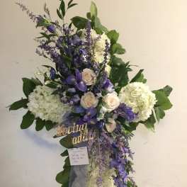 Cross-shaped floral tribute with white hydrangeas, purple flowers, and roses