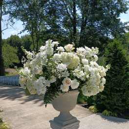 Large white floral arrangement in a pedestal urn outdoors