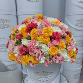 Round bouquet of pink, yellow, white, and lavender roses in a white hat box