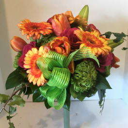 Bouquet of orange and pink flowers in a tall glass vase with a green ribbon