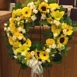 Heart-shaped yellow floral wreath on a stand with a white ribbon