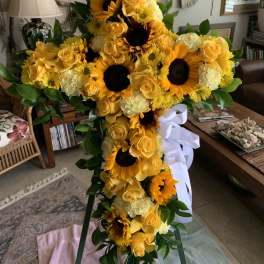 Tall yellow floral standing spray with sunflowers, roses, and a white ribbon