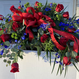 Red roses and blue flowers in a white container with a red ribbon