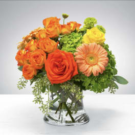 Bright orange and yellow roses with a peach gerbera daisy in a clear glass vase