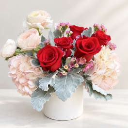 Red roses and pale pink flowers arranged in a white vase