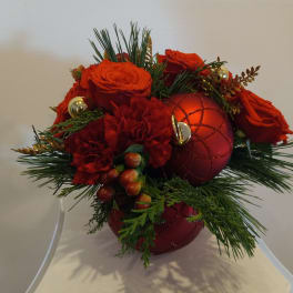 Red roses and carnations arranged with holiday ornaments in a vase