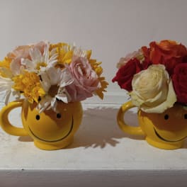 Two yellow smiley-face mugs filled with mixed flowers