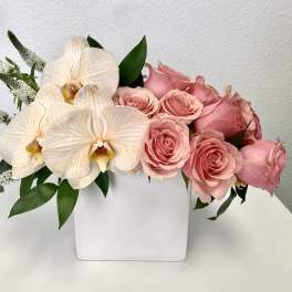 Pink roses and white orchids arranged in a white square vase