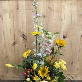 Tall floral arrangement with yellow roses, sunflowers, and white snapdragons in a white box