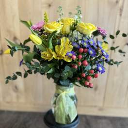 Bouquet of yellow roses, purple daisies, and pink blooms in a glass vase