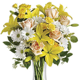 Yellow lilies and peach roses in a clear glass vase