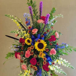 Tall multicolor standing spray with sunflowers, roses, carnations, and snapdragons on an easel