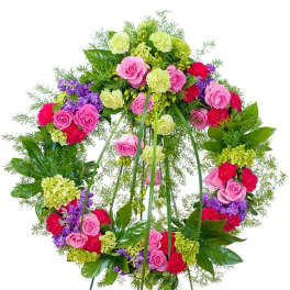 Standing wreath of pink roses, green carnations, and purple blooms on a metal easel.