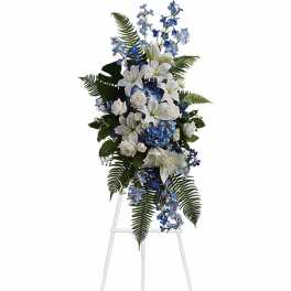 Tall standing spray of white lilies and roses with blue flowers on a white easel