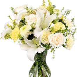 White lilies, cream roses, and pale yellow blooms arranged in a clear glass vase