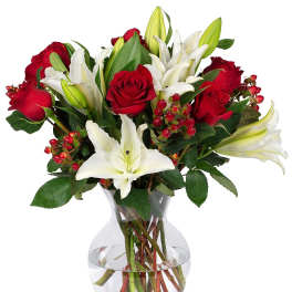 Red roses and white lilies arranged with red berries in a clear glass vase