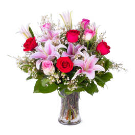Glass vase arrangement with pink lilies, red and pink roses, and small white filler flowers