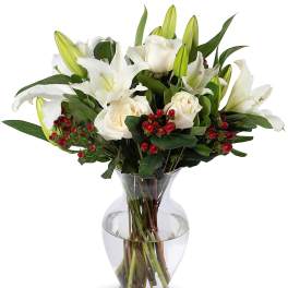 White lilies and roses with red berries arranged in a clear glass vase