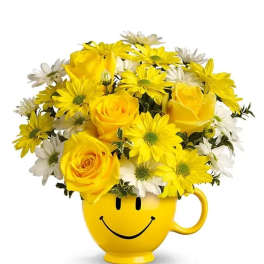 Yellow roses and white and yellow daisies arranged in a yellow smiley-face mug.