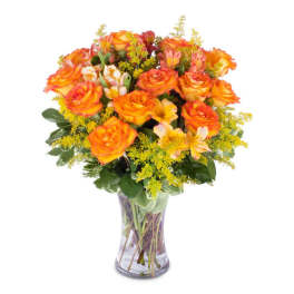 Arrangement of orange roses and yellow flowers in a clear glass vase