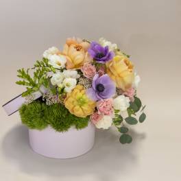 Pastel flower arrangement in a round pink box with purple and peach blooms
