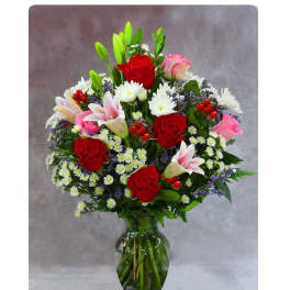 Tall mixed bouquet of red roses, pink lilies, and white daisies in a clear glass vase