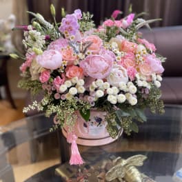 Pink mixed flower arrangement in a round hatbox with a tassel