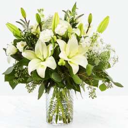 Arrangement of white lilies and white blooms in a clear patterned glass vase