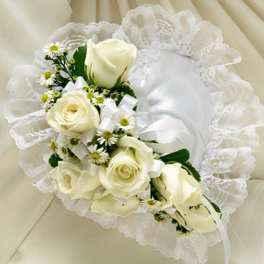 White roses and small white daisies arranged on a satin pillow with lace trim and white ribbons