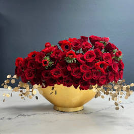 Red rose arrangement in a gold bowl with trailing dried foliage