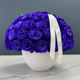 Purple rose arrangement in a white vase with a ribbon