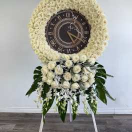 White rose funeral wreath with a clock centerpiece on a stand