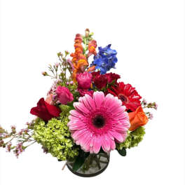 Mixed bouquet with pink gerbera, roses, and blue flowers in a glass vase