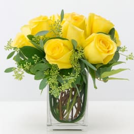 Yellow roses arranged in a clear glass vase with greenery