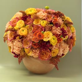 Round bouquet of yellow, peach, and orange flowers in a vase