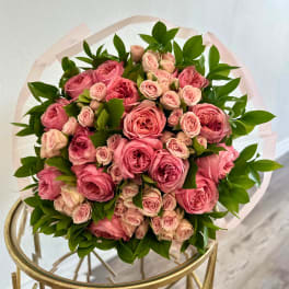Round bouquet of pink roses with green foliage wrapped in pale paper