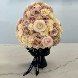 Round bouquet of blush and cream roses in a black ribbon-wrapped base