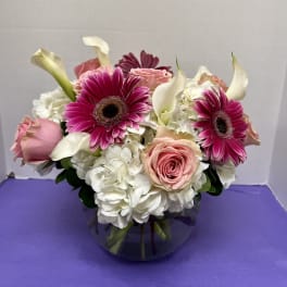 Pink gerberas, roses, white hydrangeas, and calla lilies in a glass vase