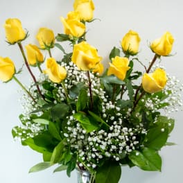 Tall arrangement of yellow roses with white filler flowers in a clear glass vase