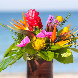 Tropical bouquet with bird of paradise, pink blooms, and yellow pincushion flowers in a vase