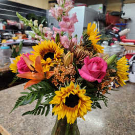 Mixed bouquet with sunflowers, pink roses, lilies, and snapdragons in a glass vase