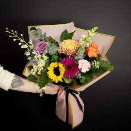 Mixed bouquet with sunflower, roses, and chrysanthemums wrapped in pink paper