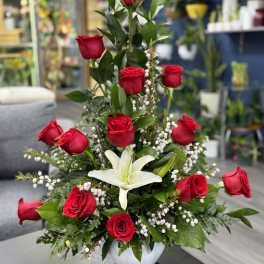 Tall arrangement of red roses and a white lily in a white vase