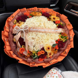 Round bouquet of cream, orange, and burgundy flowers with a ribbon bow