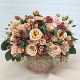 Basket arrangement of blush and mauve roses with greenery