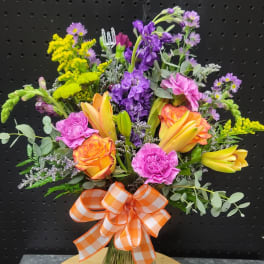 Mixed bouquet of orange roses, yellow lilies, and purple flowers in a glass vase