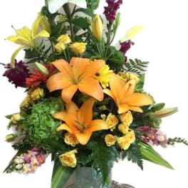 Tall mixed flower arrangement with lilies, roses, and snapdragons in a glass vase