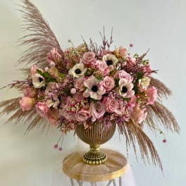 Pink rose and anemone arrangement in a gold vase with feathery pampas grass