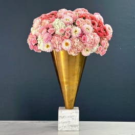 Pink floral arrangement in a gold cone vase on a marble base