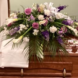 Floral casket spray with pink roses, white lilies, and purple flowers